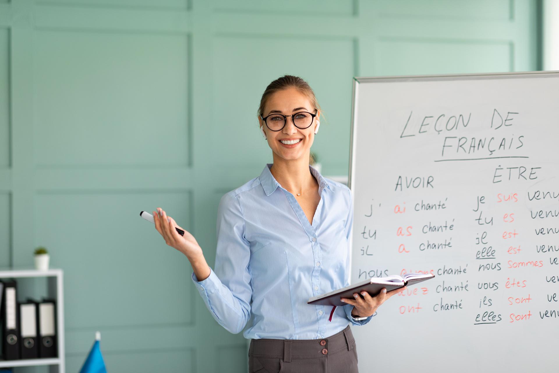 Professeur amical et heureux recommandant une école de langues étrangères, donnant Français leçon, se tenant près du tableau blanc et souriant