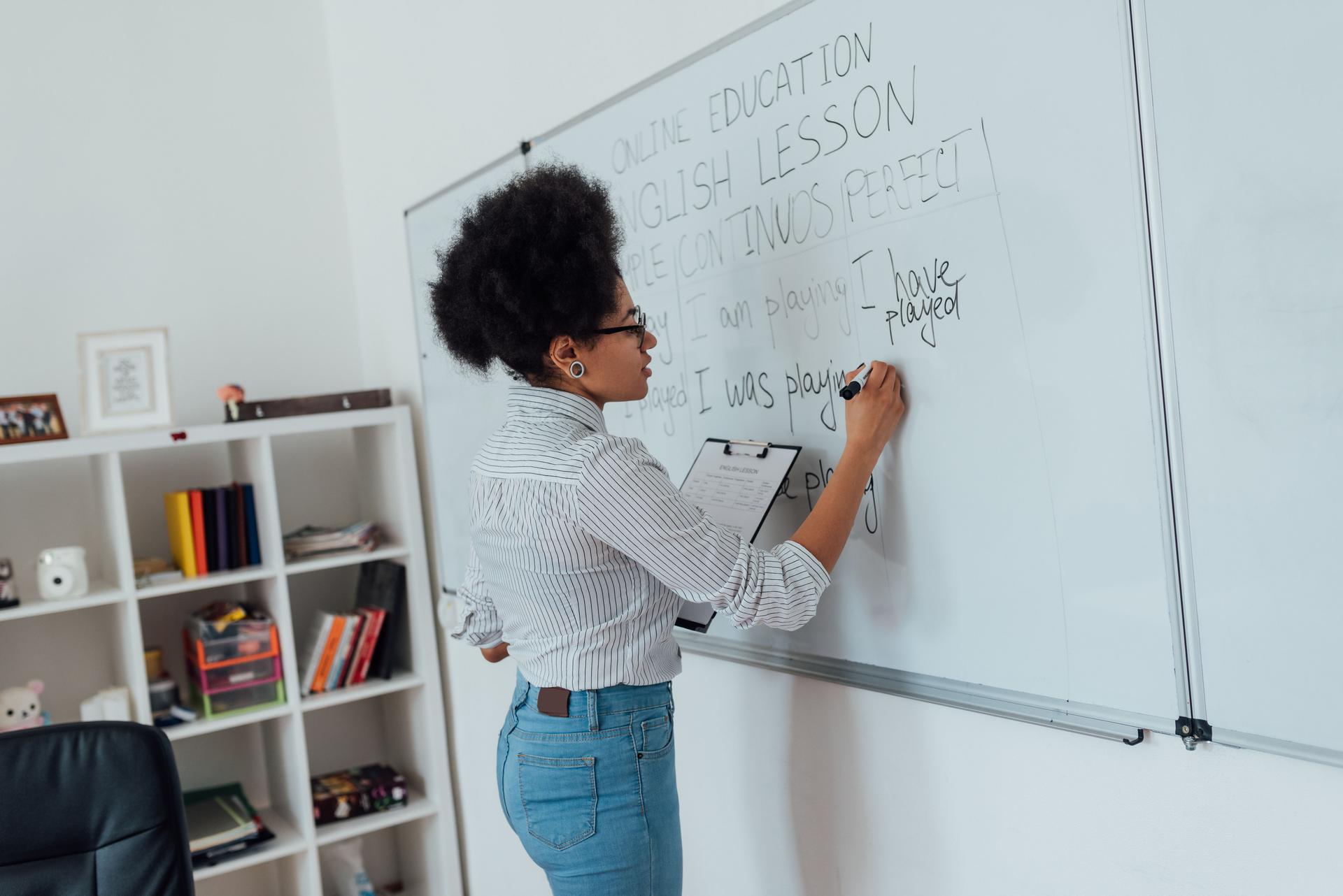 École en ligne. Vue latérale d’une jeune professeur afro-américaine d’écriture d’écriture sur le tableau blanc et d’enseignement de la langue anglaise par internet de la maison