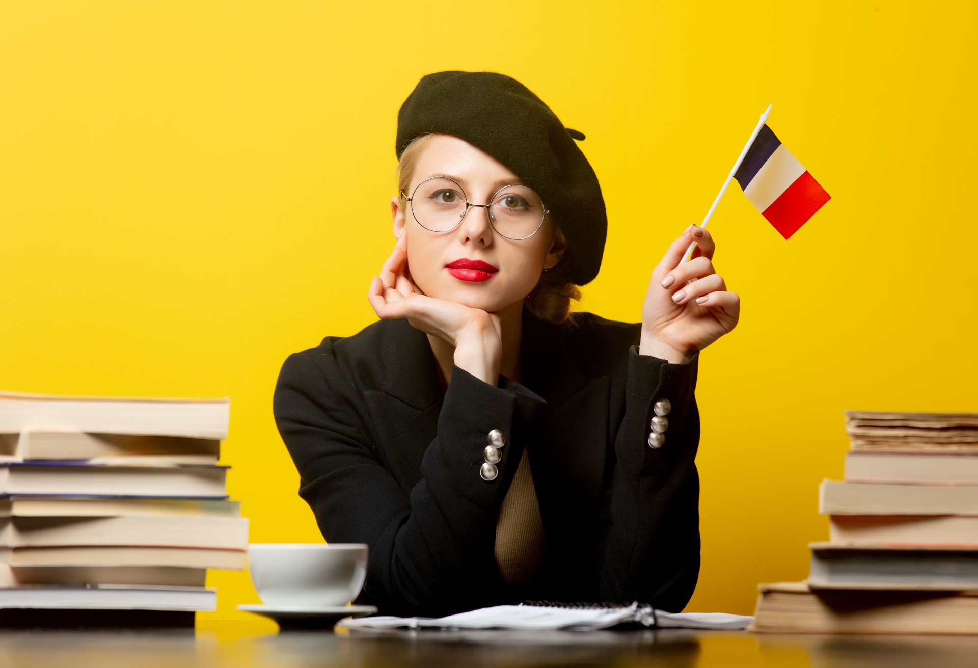 Femme blonde de modèle dans le béret avec le drapeau Français et les livres autour sur le fond jaune